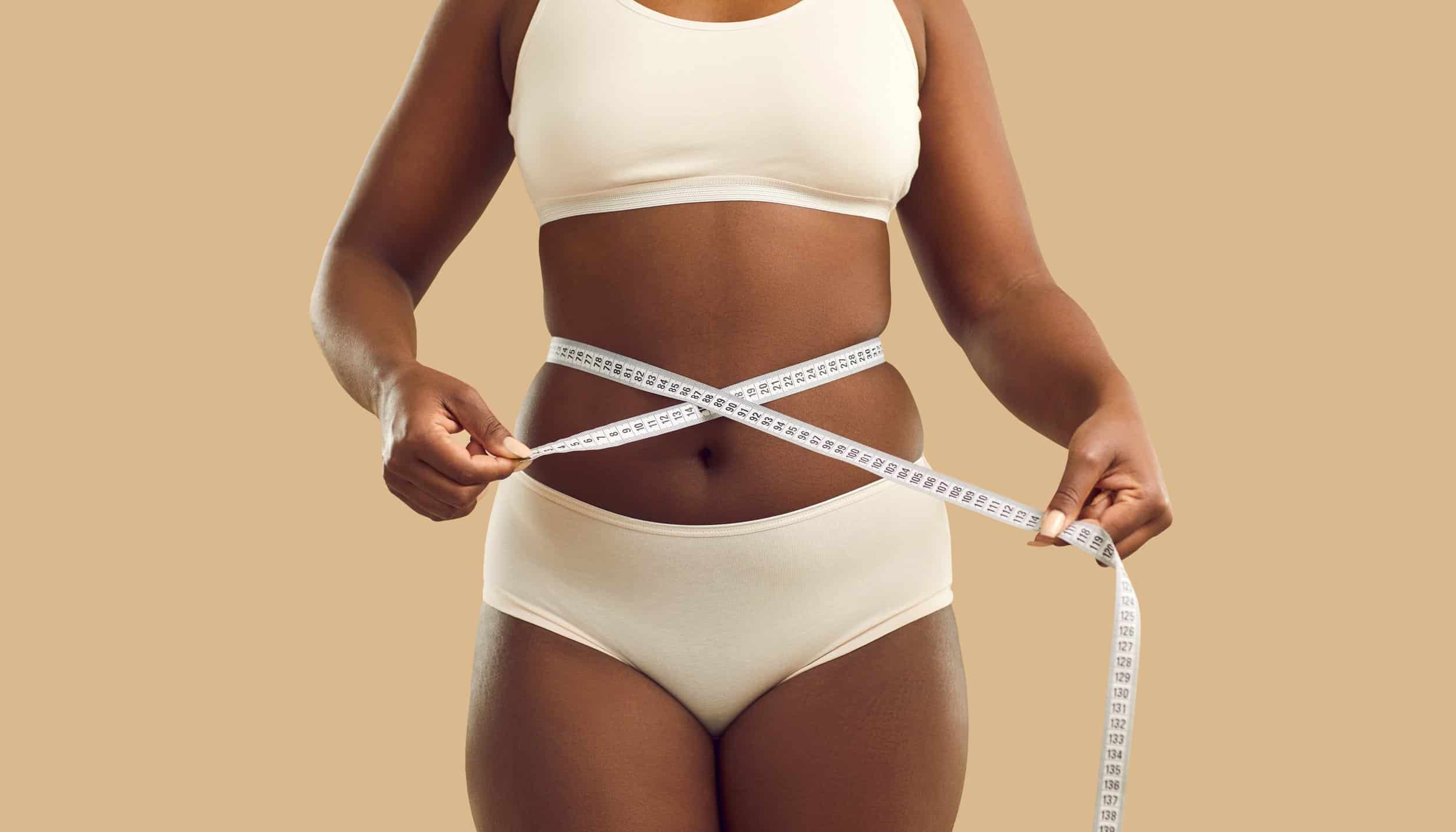 Black woman in underwear measure waist with tape